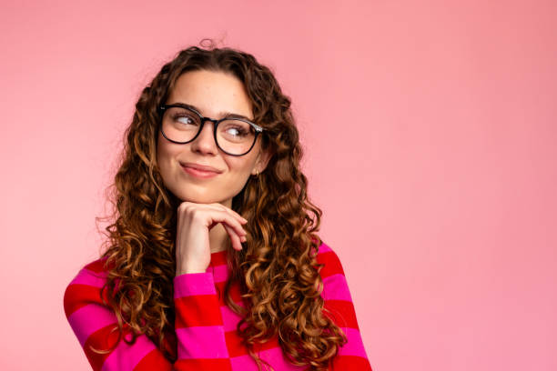 Thoughtful young woman with glasses looking up on a pink background. tendencias de gafas en 2025